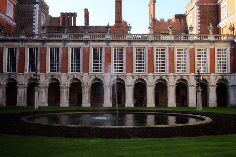 The image depicts the facade of a large, historic building with a classical architectural style, featuring an elaborate stone pediment with decorative relief sculptures at the center, supported by tal